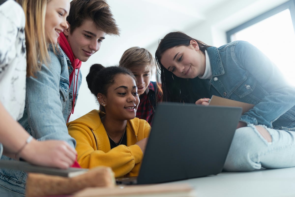 High school students sitting together at s desk and using laptop and talking during break in classroom