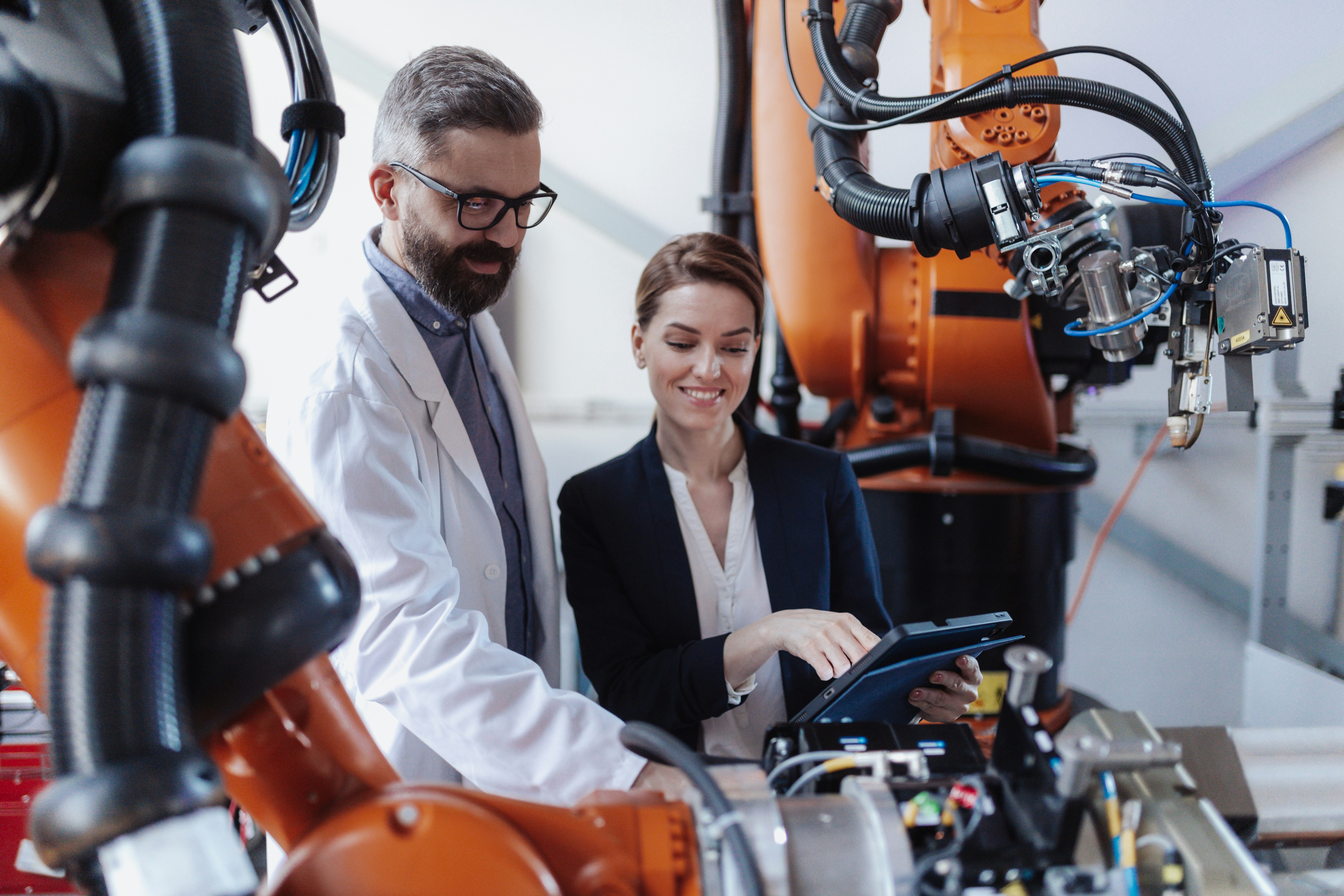 Robotics engineers with a tablet discussing and designing a modern robotic arm in a factory.